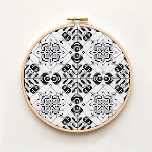 Peut inclure: Broderie au point de croix terminée, présentée dans un cercle en bois. Le motif géométrique noir et blanc est répété, avec des formes symétriques et des lignes détaillées, créant un design complexe.