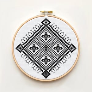 Peut inclure: Un tambour à broder circulaire en bois contenant un tissu blanc avec un motif de point de croix noir. Le design présente une grande forme de losange centrale composée de motifs géométriques complexes, incluant des losanges plus petits.