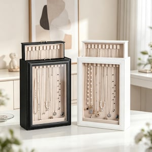 May include: Two rectangular jewelry display cases, one black and one white, featuring a clear front panel and a top compartment. Each case has a beige interior with multiple hooks for hanging necklaces, providing an organized storage solution.