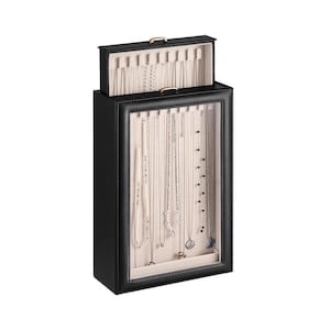 May include: A black jewelry organizer with a clear front, showcasing various necklaces. The top section is open, revealing additional storage. The interior is a light beige, providing a contrast to the dark exterior. The organizer has a gold-colored handle.