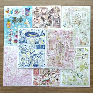 May include: A collection of decorative sticker sheets featuring various themes. Designs include tropical scenes with palm trees and pineapples, celestial patterns with stars and moons, and floral arrangements. The color palette includes blues, pinks, and greens.