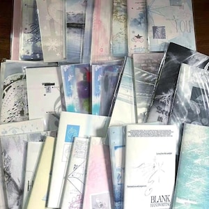 May include: A selection of bookmarks, many in clear plastic packaging. The bookmarks display watercolour designs in blue, pink, and white, with some including text and illustrations. The theme is stationery and paper goods.