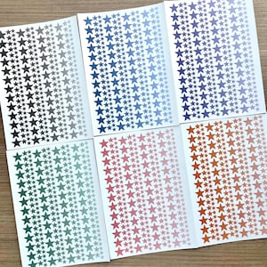 May include: Six rectangular sheets of adhesive star stickers, each featuring a gradient colour scheme. The sheets display rows of stars in varying sizes, ranging from dark to light shades of grey, blue, purple, green, pink, and orange.