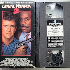 May include: A VHS tape of the movie "Lethal Weapon 2" featuring Mel Gibson and Danny Glover. The box art displays the film's title and the actors' faces. The VHS tape is black with a white label.