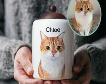 May include: A white ceramic pet urn with a detailed portrait of a tabby cat. The urn has a dark brown wooden lid and the name "Chloe" is written in black script. An oval portrait of the cat is next to the urn.