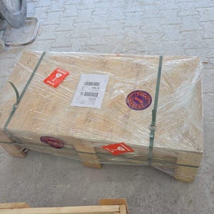 Puede incluir: Una caja de env&iacute;o rectangular de madera asegurada con correas de pl&aacute;stico verde y envuelta en film pl&aacute;stico transparente. La caja presenta una etiqueta de env&iacute;o blanca, dos pegatinas rojas de advertencia de fr&aacute;gil y dos etiquetas circulares.