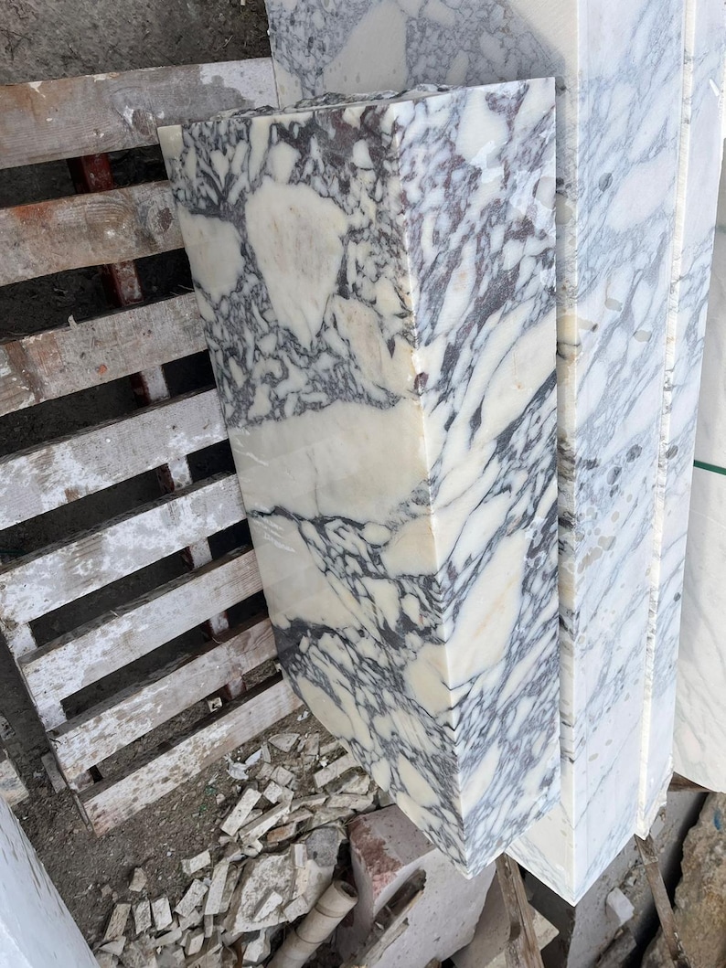 Puede incluir: Un bloque rectangular de m&aacute;rmol blanco pulido que presenta vetas irregulares de color gris oscuro y negro en toda su superficie. La losa de piedra muestra un acabado de alto brillo con un patr&oacute;n natural complejo de dep&oacute;sitos minerales.