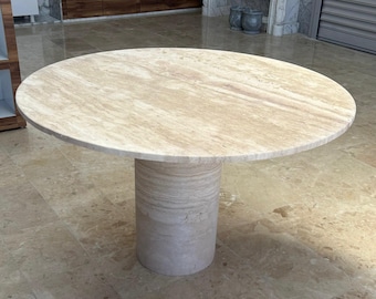 May include: A round, beige stone table with a cylindrical base. The tabletop is approximately 122 cm in diameter. The table has a natural, textured surface and is suitable for indoor use.