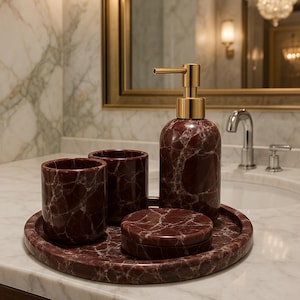 Op de afbeelding: Een badkamerset met een zeepdispenser, twee bekers, een kleine bak met deksel en een rond dienblad. De set is gemaakt van donkerrood marmer met witte aderen en goudkleurige accenten. De items zijn gerangschikt op een marmeren aanrecht.