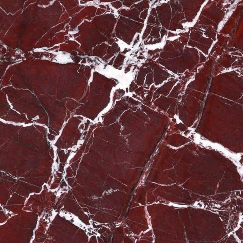 Puede incluir: Primer plano de una superficie de m&aacute;rmol rojo con vetas blancas. La piedra tiene un acabado pulido, con un patr&oacute;n complejo de grietas y fisuras. El color es un rojo intenso y rico, con las vetas blancas creando un contraste llamativo.