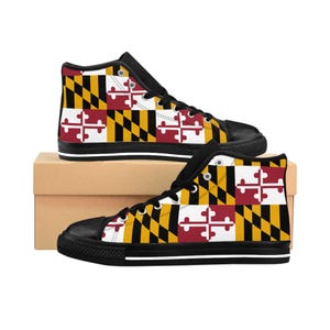 Może przedstawiać: Wysokie trampki płócienne z wzorem flagi stanu Maryland. Buty mają czarny nosek, sznurowadła i podeszwy z białym paskiem na podeszwie środkowej. Wzór flagi Maryland obejmuje czarne i złote romby oraz czerwone i białe krzyże.