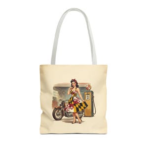 Może przedstawiać: Kremowa torba typu tote z ilustracją w stylu vintage przedstawiającą kobietę w sukience z motywem flagi Maryland, stojącą obok motocykla i dystrybutora paliwa. Torba ma białe paski i estetykę retro.