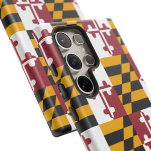 Może przedstawiać: Dwa etui na telefon z powtarzającym się wzorem flagi stanu Maryland. Wzór przedstawia białe tło z czerwonymi i czarnymi geometrycznymi kształtami oraz żółto-czarny wzór szachownicy. Etui na telefon mają czarny moduł aparatu.