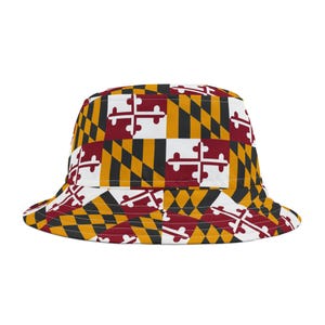 Puede incluir: Sombrero de pescador con un patrón repetido de la bandera del estado de Maryland. El diseño incluye los símbolos de la cruz y la bandera del estado en blanco, rojo, negro y dorado. Un accesorio casual.