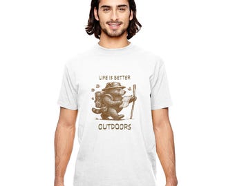 May include: White t-shirt featuring a brown illustration of a bear wearing a hat, backpack, and holding a map and walking stick. The text "LIFE IS BETTER" is above the bear, and "OUTDOORS" is below.