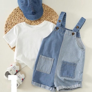 Op de afbeelding: Een set bestaande uit een effen wit t-shirt met korte mouwen, een blauwe spijkerpet, een paar witte sneakers met rode accenten en een spijkerbroek met bretels in een split-design met één effen blauwe en één blauw gestreepte kant.