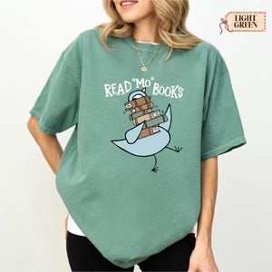 A woman wearing a green t-shirt with a graphic design of a bird carrying a stack of books.