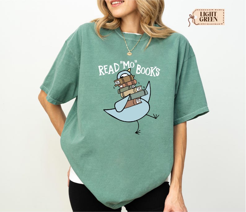 A woman wearing a green t-shirt with a graphic design of a bird carrying a stack of books.