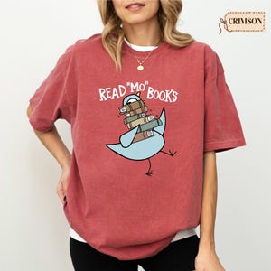 A woman wearing a red t-shirt with a graphic design of a bird carrying books.