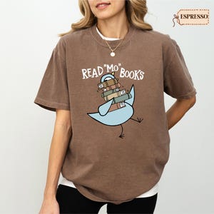 A woman wearing a brown t-shirt with a graphic design of a bird carrying a stack of books.