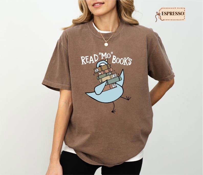 A woman wearing a brown t-shirt with a graphic design of a bird carrying a stack of books.
