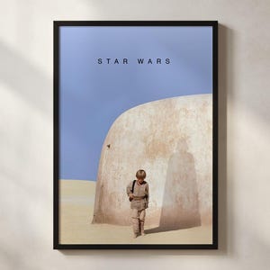 May include: Framed Star Wars poster featuring a young boy in a desert landscape. The poster has a black frame and the words "STAR WARS" are printed at the top. The boy is wearing a tan outfit and standing in front of a large, rounded structure.