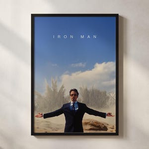 May include: Framed poster featuring a man in a suit with arms outstretched against a backdrop of a blue sky and a sand-colored landscape. The text "IRON MAN" is displayed at the top of the poster.