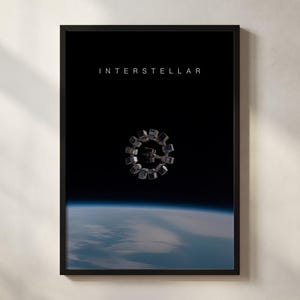 May include: Framed print with the word "INTERSTELLAR" at the top, above a space station design. The image shows a view of Earth from space, with blue and white clouds against a black backdrop.