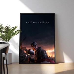 May include: Framed print featuring Captain America holding Thor's hammer, set against a fiery, war-torn background. The words "CAPTAIN AMERICA" are displayed at the top. The artwork is displayed on a wooden surface.