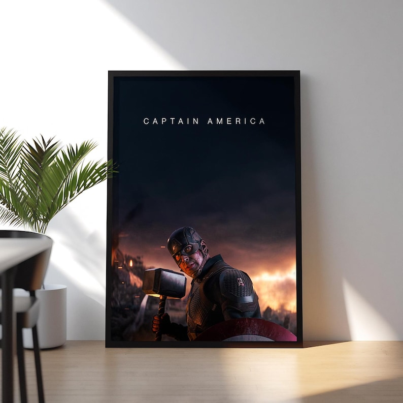 May include: Framed print featuring Captain America holding Thor's hammer, set against a fiery, war-torn background. The words "CAPTAIN AMERICA" are displayed at the top. The artwork is displayed on a wooden surface.