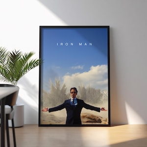 May include: Framed poster featuring the text "IRON MAN" above an image of a man in a suit with arms outstretched. The background shows a blue sky with clouds and a dusty landscape.