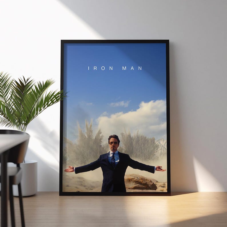 May include: Framed poster featuring the text "IRON MAN" above an image of a man in a suit with arms outstretched. The background shows a blue sky with clouds and a dusty landscape.