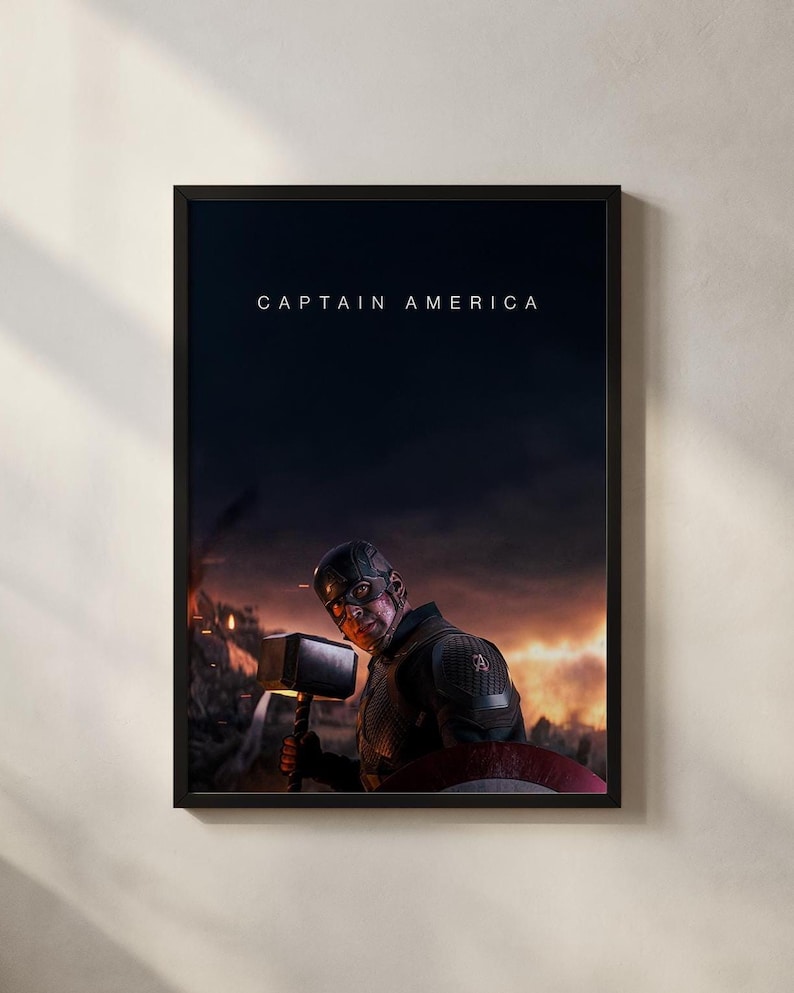 May include: Framed Captain America poster featuring the character holding a hammer and shield, with the text "CAPTAIN AMERICA" at the top. The background shows a fiery, war-torn scene. The poster is in a black frame.