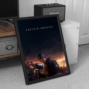 May include: Framed print featuring Captain America holding Thor's hammer, set against a fiery battle scene. The title "CAPTAIN AMERICA" is displayed in white text at the top. The print is in a black frame.