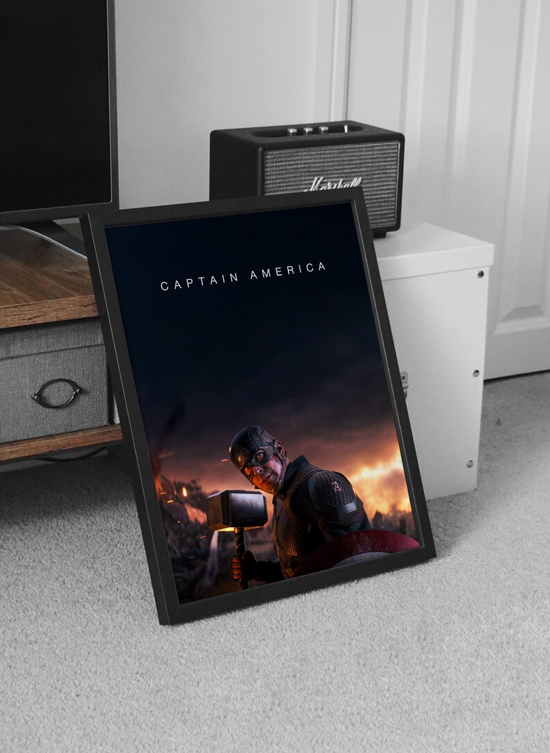 May include: Framed print featuring Captain America holding Thor's hammer, set against a fiery battle scene. The title "CAPTAIN AMERICA" is displayed in white text at the top. The print is in a black frame.