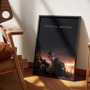 May include: Framed art print featuring Captain America holding Thor's hammer, set against a fiery, cinematic background. The title "CAPTAIN AMERICA" is displayed at the top. The artwork is leaning against a wall near a wooden chair.