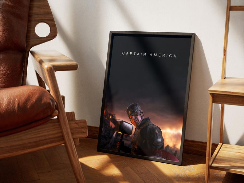 May include: Framed art print featuring Captain America holding Thor's hammer, set against a fiery, cinematic background. The title "CAPTAIN AMERICA" is displayed at the top. The artwork is leaning against a wall near a wooden chair.