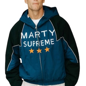 以下が含まれることがあります： 前面に白で「MARTY SUPREME」の文字と3つのオレンジ色の星が描かれた、ティール色のパネルが付いたフード付きジャケット。 ジャケットは、黒い上背と袖、白いトリム、シルバーのジッパーを備えています。