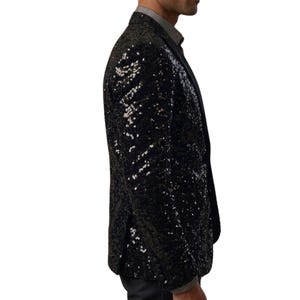 Pode incluir: Um blazer preto com lantejoulas e lapela entalhada. O casaco &eacute; coberto por pequenas lantejoulas refletoras, criando um efeito brilhante. O blazer &eacute; usado sobre uma camisa com colarinho.