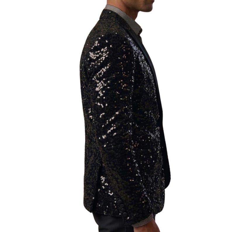 Pode incluir: Um blazer preto com lantejoulas e lapela entalhada. O casaco &eacute; coberto por pequenas lantejoulas refletoras, criando um efeito brilhante. O blazer &eacute; usado sobre uma camisa com colarinho.