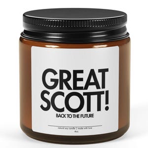May include: A brown glass jar with a black lid. The jar has a white label with the text "GREAT SCOTT!" in bold black letters, with "BACK TO THE FUTURE" below. The candle is a natural soy candle and made with love.