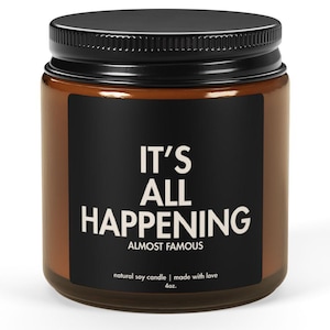 Puede incluir: Un tarro de vidrio marrón con tapa negra y etiqueta negra. La etiqueta dice "IT'S ALL HAPPENING" en texto blanco. El tarro contiene una vela de soja natural.