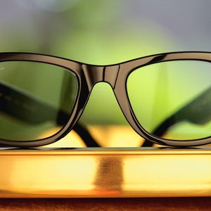 Puede incluir: Gafas inteligentes con montura negra y lentes de color verde. Las gafas tienen un dise&ntilde;o cl&aacute;sico con un toque moderno, con peque&ntilde;os detalles circulares en las patillas. El logotipo de Ray-Ban es visible en la lente.