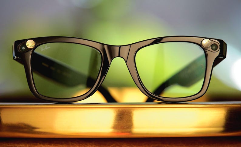 Puede incluir: Gafas inteligentes con montura negra y lentes de color verde. Las gafas tienen un dise&ntilde;o cl&aacute;sico con un toque moderno, con peque&ntilde;os detalles circulares en las patillas. El logotipo de Ray-Ban es visible en la lente.