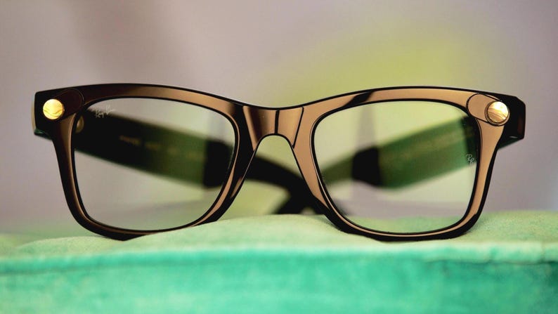 Puede incluir: Un par de gafas con montura marr&oacute;n oscuro y lentes transparentes. La montura tiene forma rectangular con bordes redondeados y detalles dorados en las patillas. Las gafas est&aacute;n sobre una superficie verde claro.