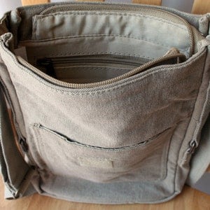 May include: A beige canvas crossbody bag with a zippered top closure and a front pocket. The bag has a long adjustable strap.