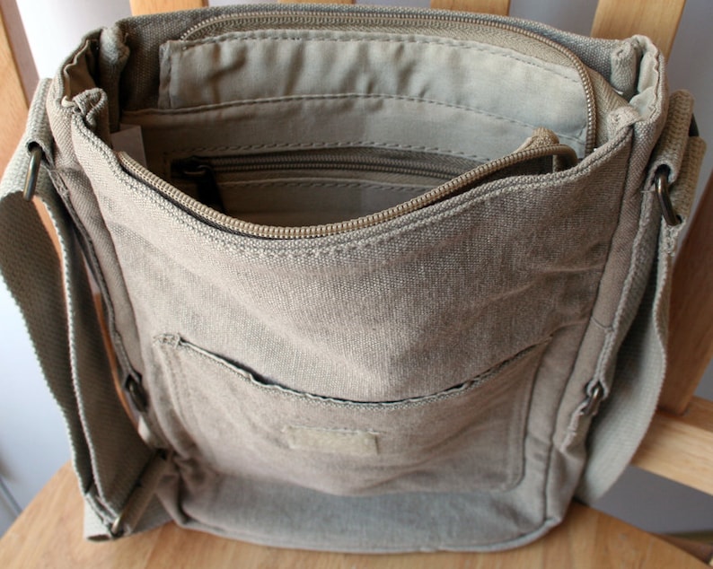 May include: A beige canvas crossbody bag with a zippered top closure and a front pocket. The bag has a long adjustable strap.