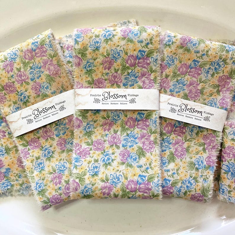 May include: Three pieces of floral fabric ribbon with a frayed edge. Each ribbon has a label that reads "Prairie Blossom Vintage, Serve Restore Believe".