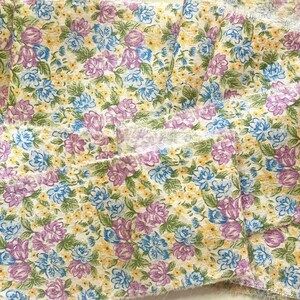 May include: A close-up of a fabric with a floral pattern. The fabric is white with small purple, blue, and yellow flowers. The fabric is folded in several layers.