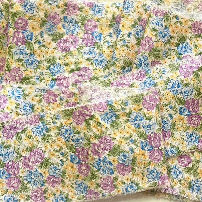May include: A close-up of a fabric with a floral pattern. The fabric is white with small purple, blue, and yellow flowers. The fabric is folded in several layers.